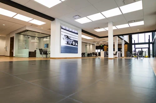 Spacious, modern office interior with polished gray floors, glass-walled conference room, and a large race car image on a pillar.